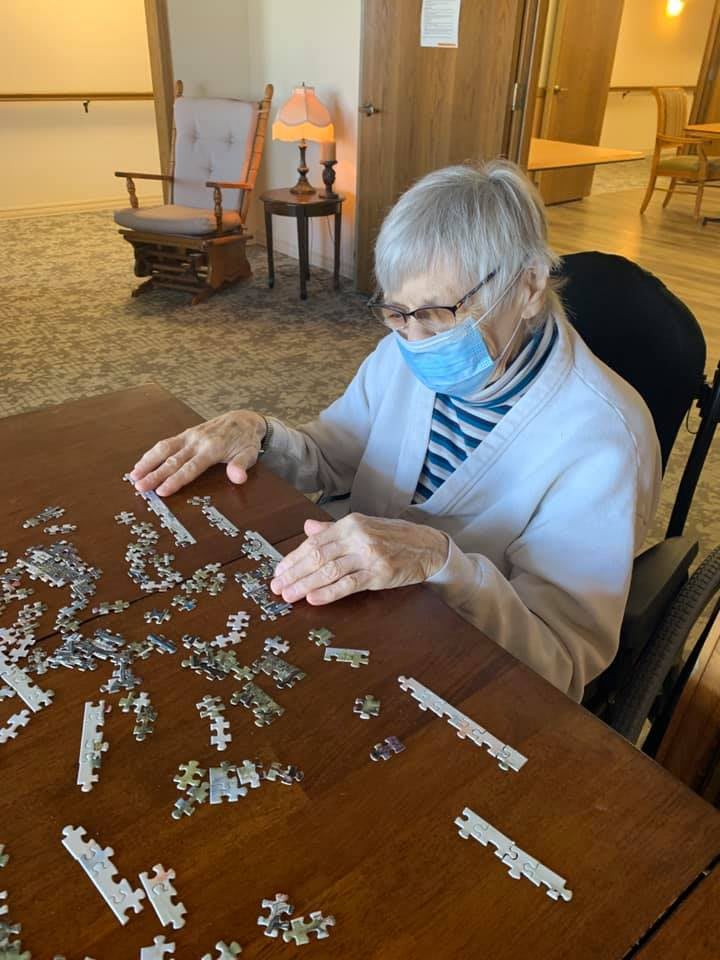 An elderly person working on a puzzle at a table while wearing a mask.