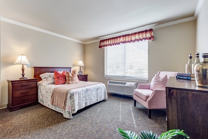 A cozy hotel room with a bed, chair, and window with curtains.