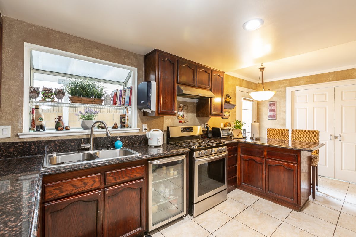 A modern kitchen with dark wooden cabinets, stainless steel appliances, and a tiled floor.