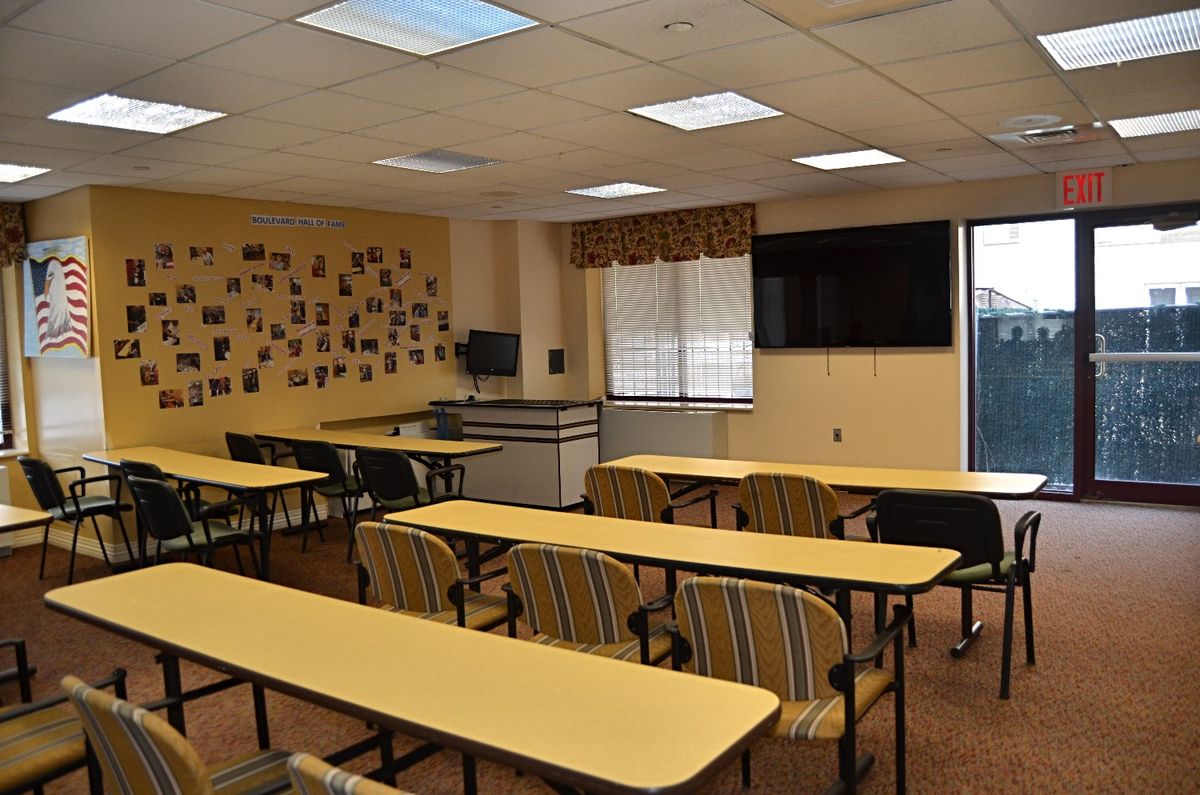 An empty classroom with desks, chairs, and a TV on the wall.