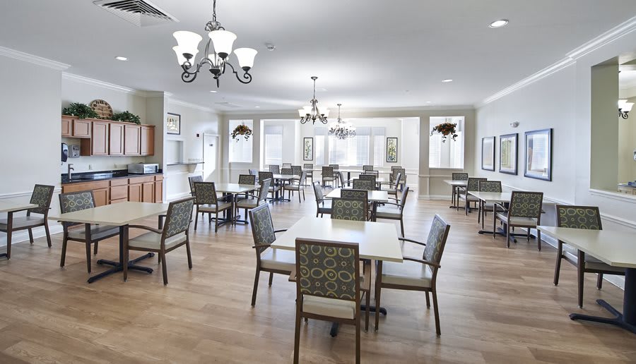 A spacious and elegantly designed dining area with multiple tables and chairs, featuring chandeliers and a wooden floor.