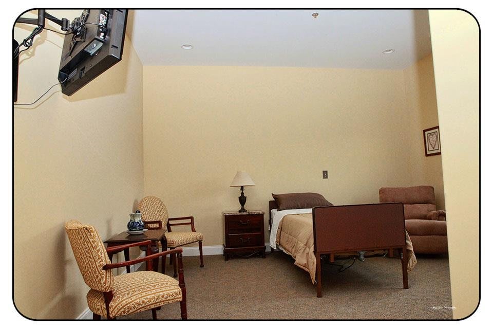 A simple bedroom with a single bed, chairs, and a lamp.