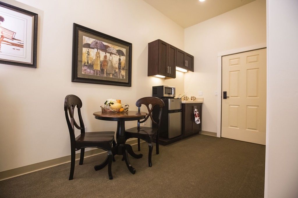 A cozy kitchenette area with a small dining table and chairs, featuring a microwave and refrigerator, accented by a decorative painting on the wall.