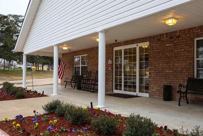 A welcoming building entrance with a porch featuring columns, a brick facade, and neatly arranged landscaping.