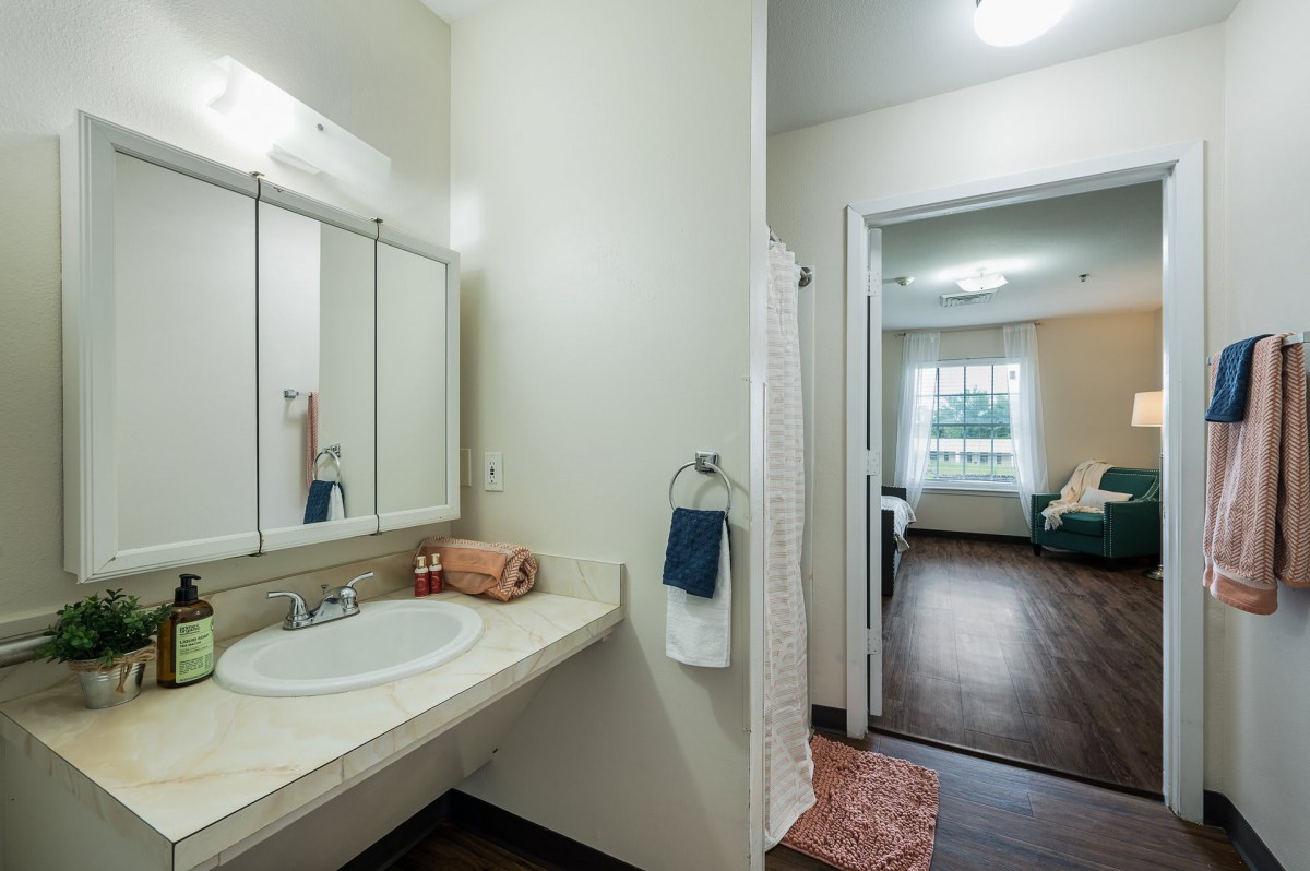 A modern bathroom with a view into a connected bedroom.