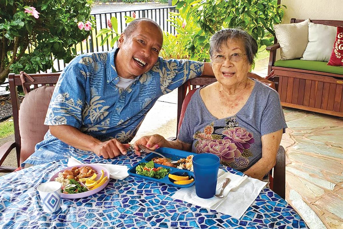 A cheerful moment shared by two people enjoying a meal outdoors in a tropical setting.