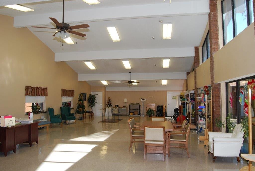 A spacious lobby area with tables, chairs, and ceiling fans under fluorescent lighting.