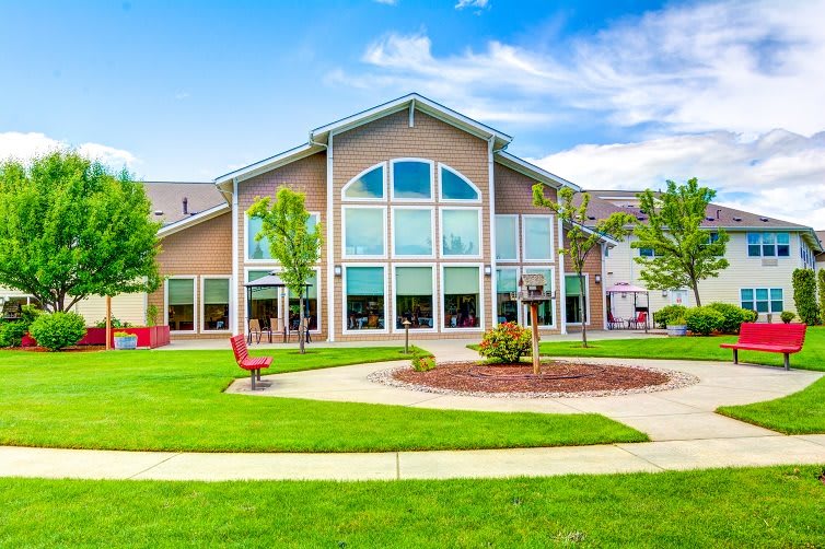 A modern building with large windows and a well-maintained lawn surrounded by trees and pathways on a clear day.