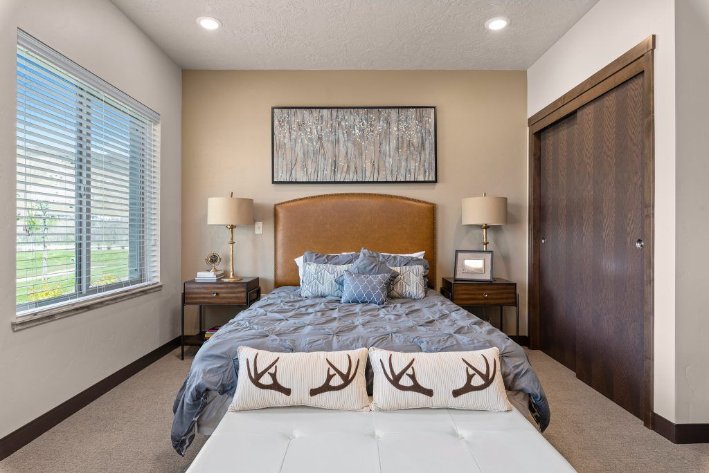 A cozy and well-decorated bedroom featuring a bed with antler-themed pillows, flanked by matching nightstands and lamps, with a large window allowing natural light.