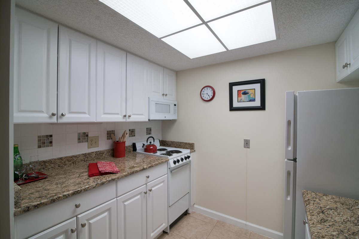 A small kitchen with white cabinets, granite countertops, and a compact stove, illuminated by overhead lighting.