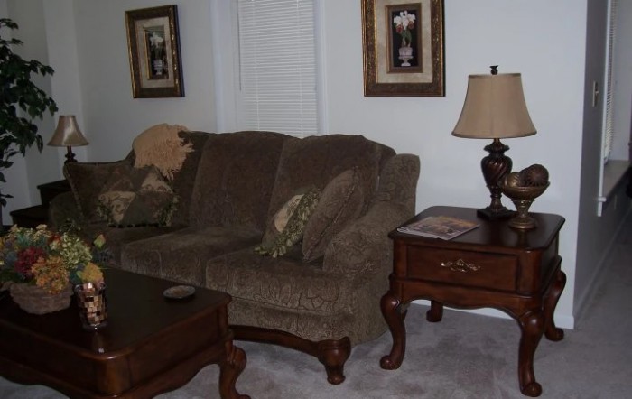 A cozy living room with a plush sofa, decorative pillows, an elegant lamp on an end table, and framed artwork.