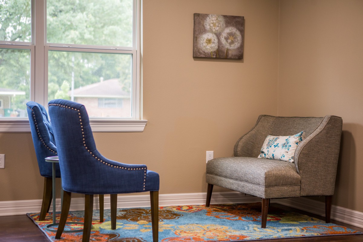 A cozy living room corner with a blue chair, gray sofa, and colorful rug.