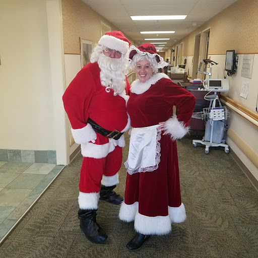 A cheerful Santa and Mrs. Claus spreading holiday joy in a hospital setting.