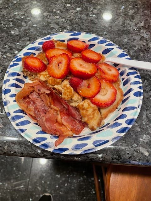 A delicious breakfast plate featuring pancakes topped with sliced strawberries and walnuts, accompanied by crispy bacon.