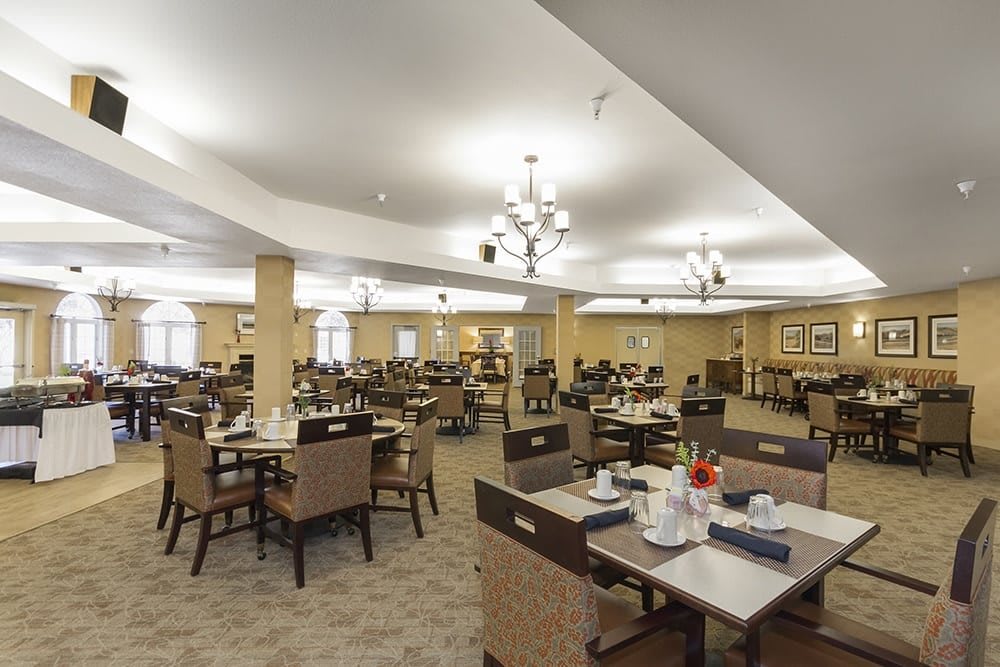 A spacious dining hall with neatly arranged tables and chairs, illuminated by chandeliers.