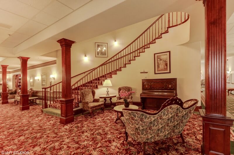 A vintage-style lounge area featuring a staircase, upholstered furniture, and a piano.