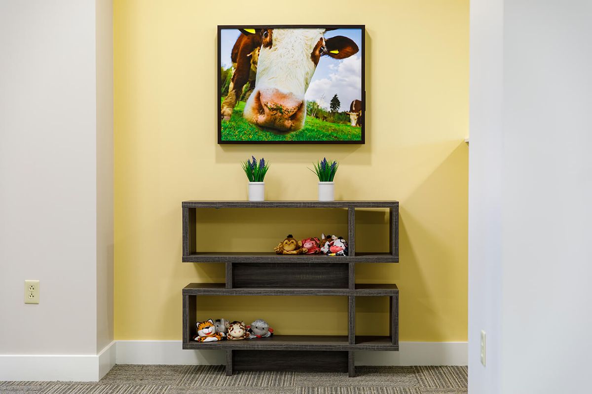 A modern interior with a cow painting, decorative plants, and a stylish shelf against a yellow wall.