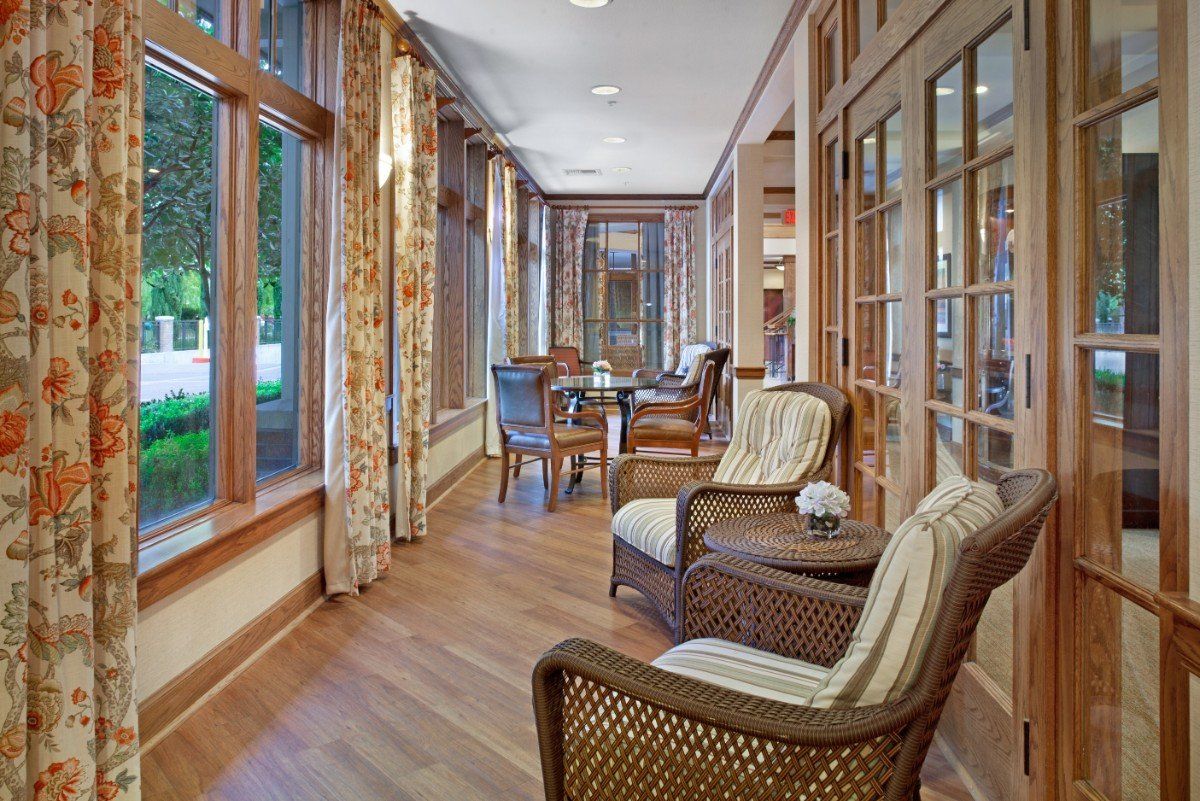 A cozy sunroom featuring rattan chairs and a wooden floor, with large windows offering ample natural light.