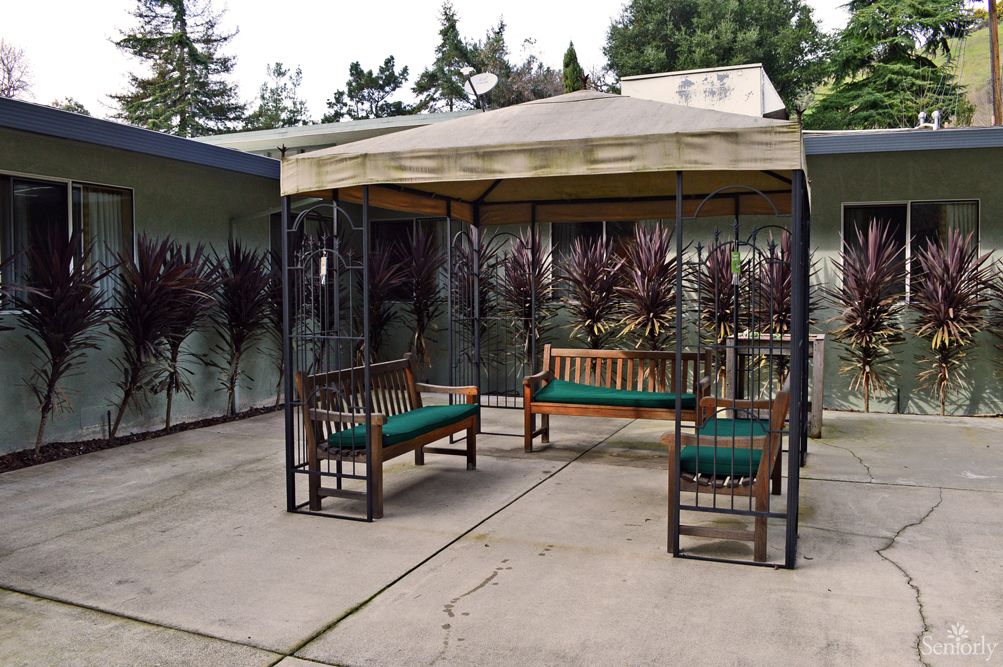 A cozy patio with a gazebo and wooden benches featuring green cushions.