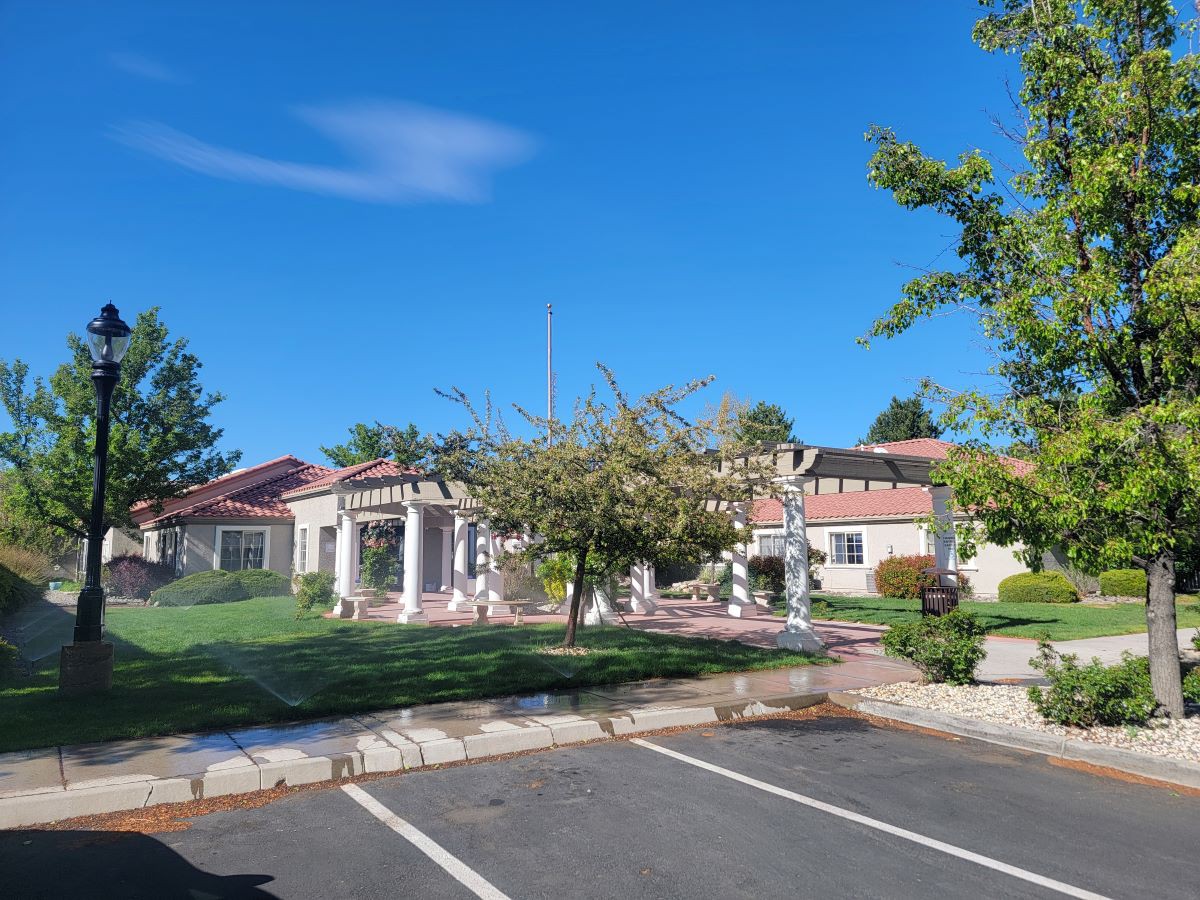 A sunny day view of a building surrounded by trees, with an empty parking lot in the foreground.