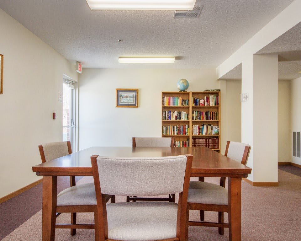 A modern meeting room with a wooden table, chairs, and a bookshelf filled with books.