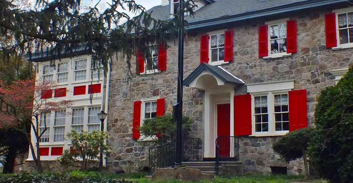 A charming stone house with red shutters and a sloped roof.