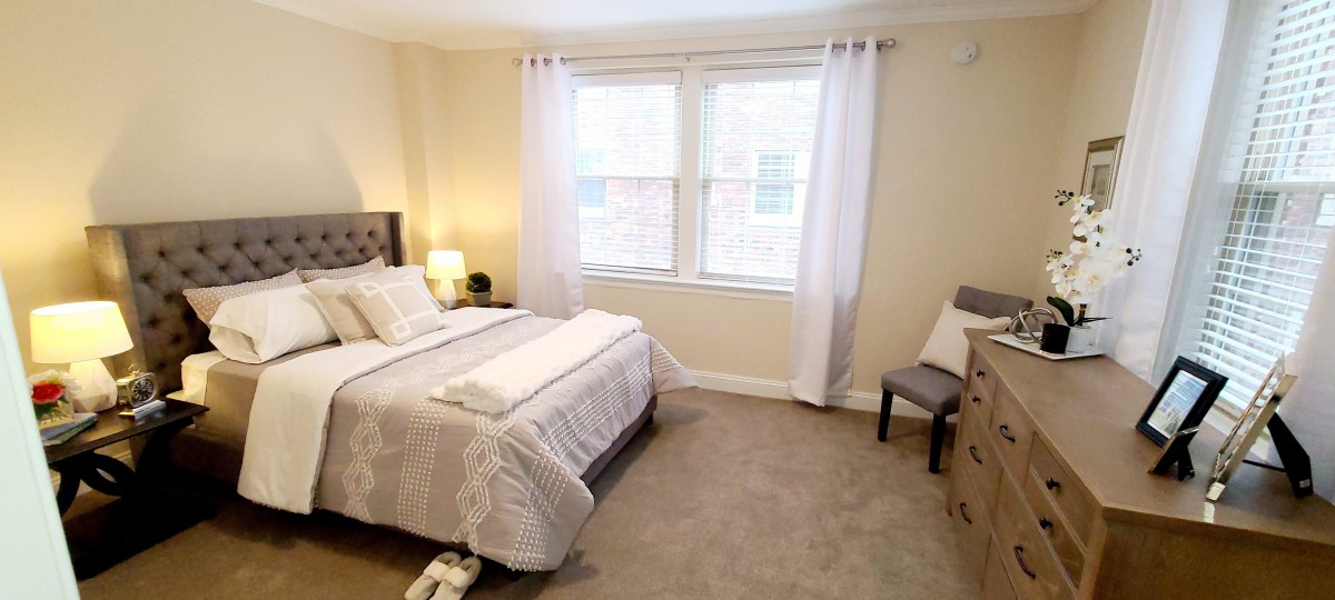 A cozy and well-decorated bedroom with a neatly made bed, soft lighting, and a window with white curtains.