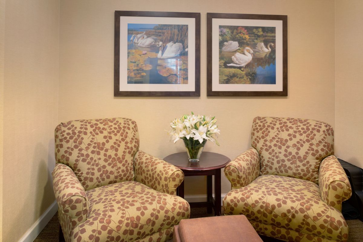 A cozy waiting room with patterned chairs, a small table with flowers, and framed artwork on the wall.