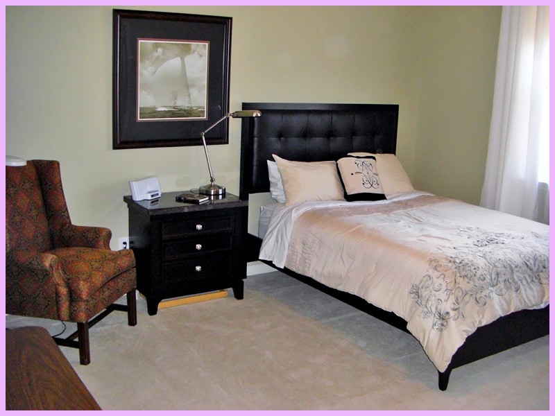 A neatly arranged bedroom with a bed, nightstand, chair, and artwork on the wall.