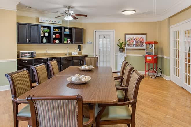 A cozy dining area featuring a long table with chairs, a ceiling fan, and a popcorn machine in the corner.