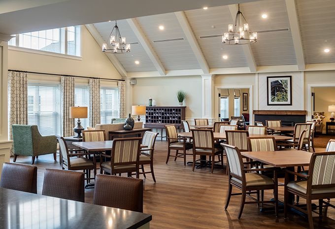 A spacious and well-lit dining room with multiple tables and chairs, elegant chandeliers, and large windows.