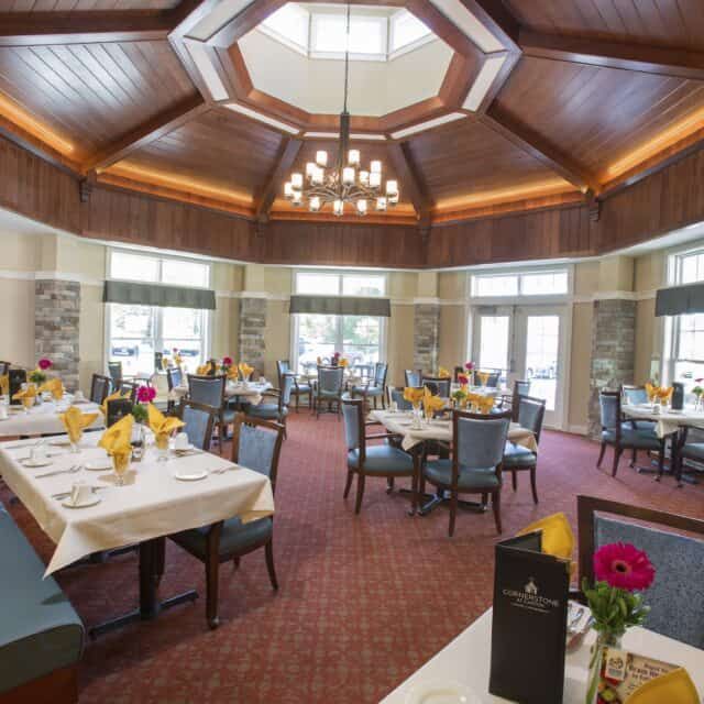 A well-lit dining room with neatly arranged tables and chairs under a chandelier.