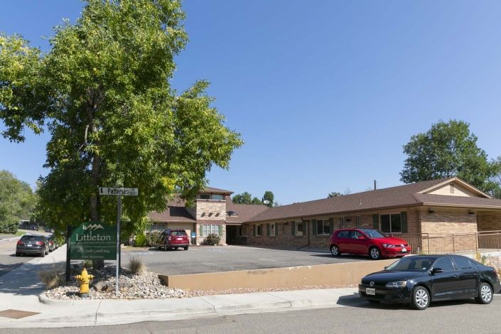 A small building with a parking lot, surrounded by trees on a sunny day.