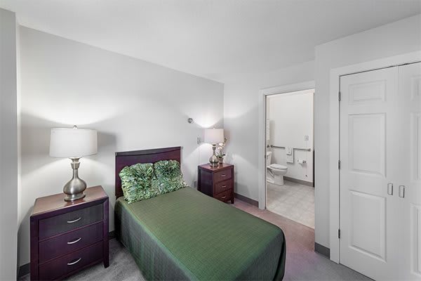 A cozy bedroom with a single bed and green bedding, featuring a connected bathroom.