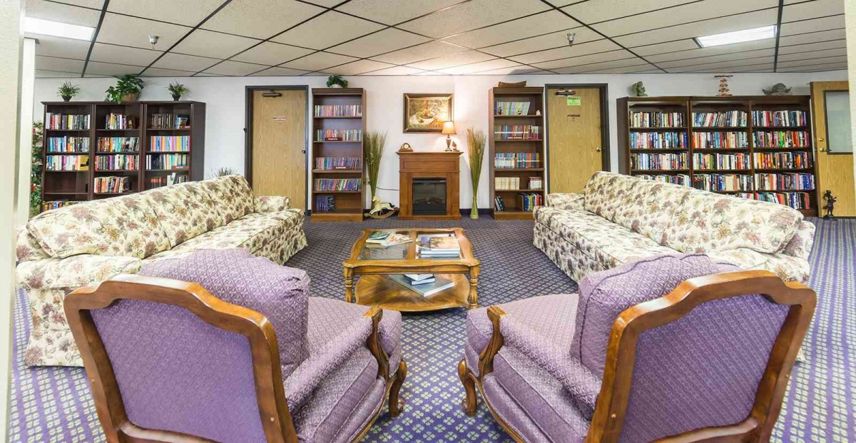 A cozy living room with sofas, armchairs, and bookshelves lining the walls.