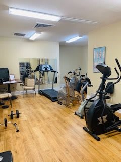 A small indoor gym with various exercise equipment including a treadmill, stationary bike, and weights.