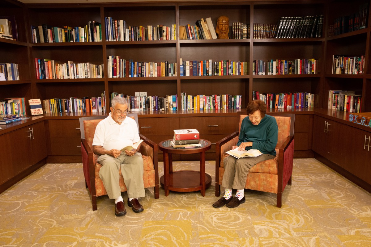 An elderly couple reading in a cozy library setting surrounded by books.