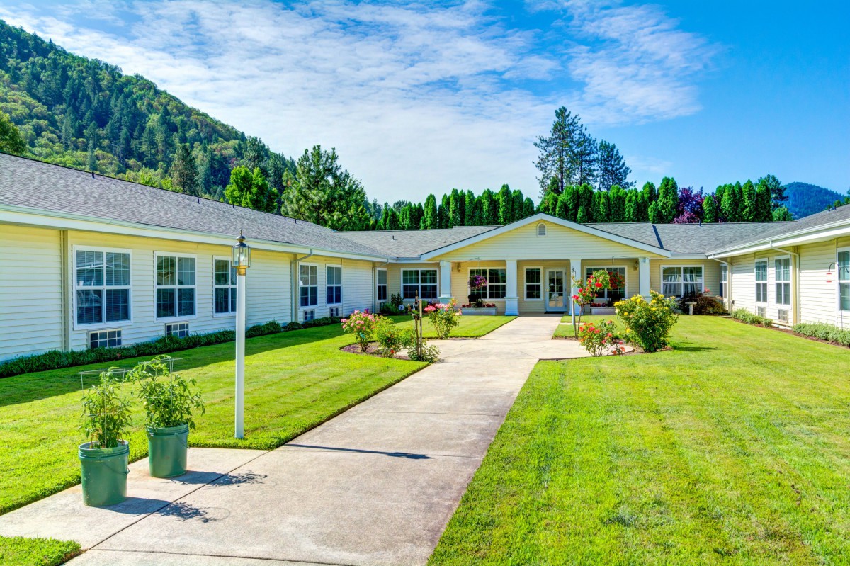 A large, single-story residential building surrounded by a well-maintained lawn and garden.