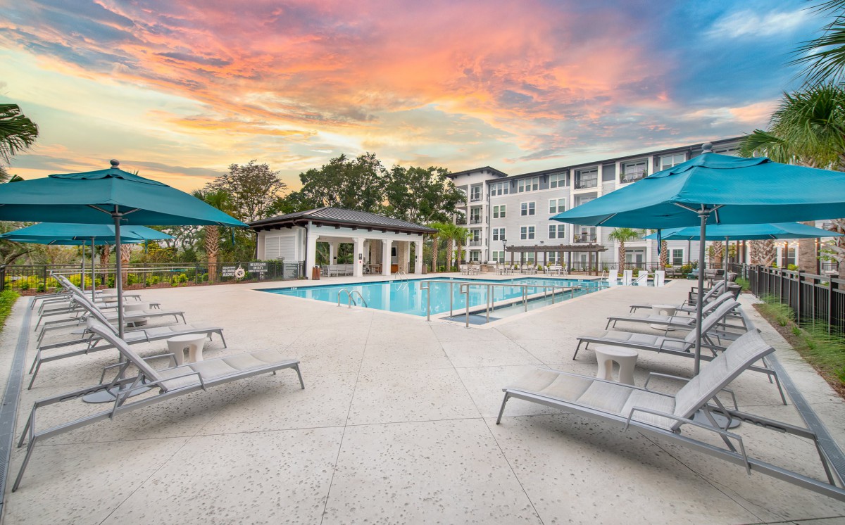 A tranquil swimming pool area at sunset, featuring lounge chairs and umbrellas, perfect for relaxation.