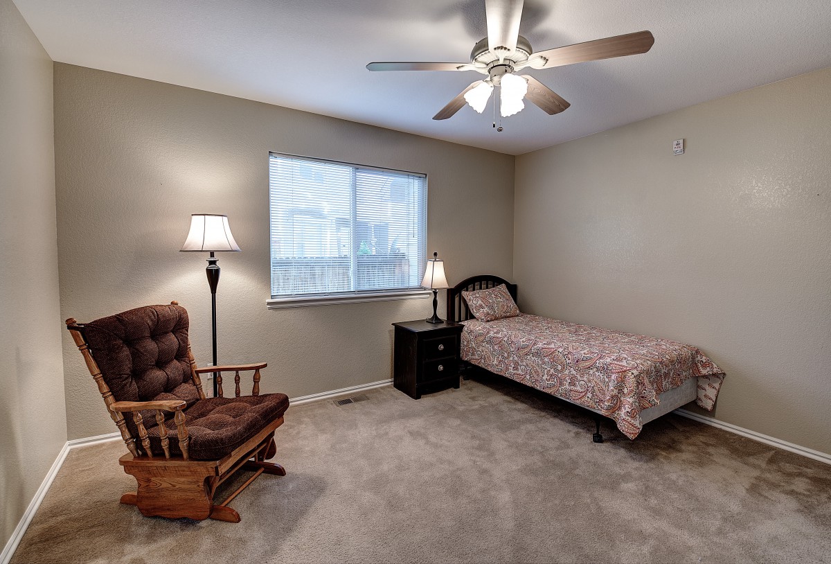 A cozy bedroom with a single bed, rocking chair, and lamp under a ceiling fan.