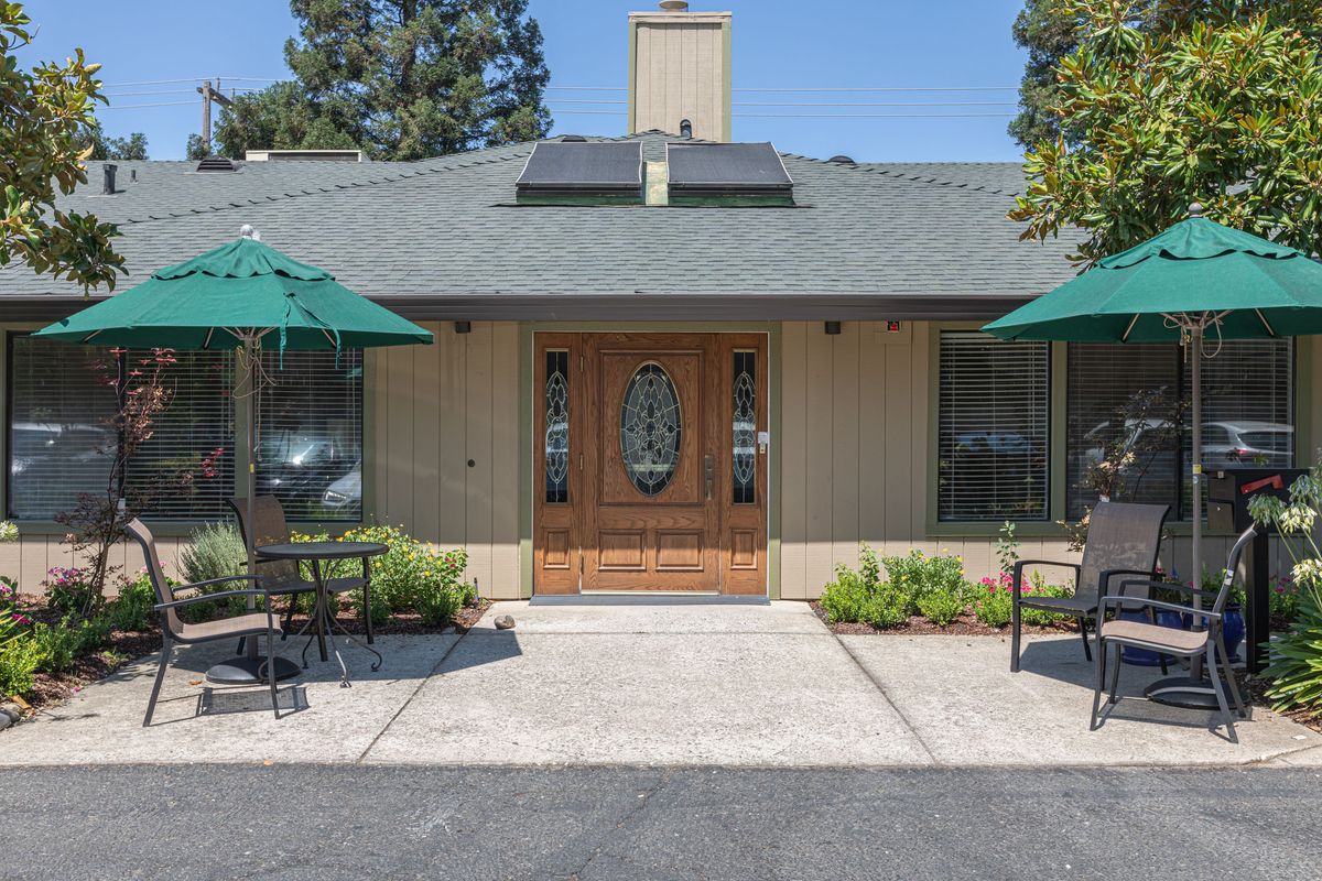 A quaint building entrance with outdoor seating and green umbrellas.