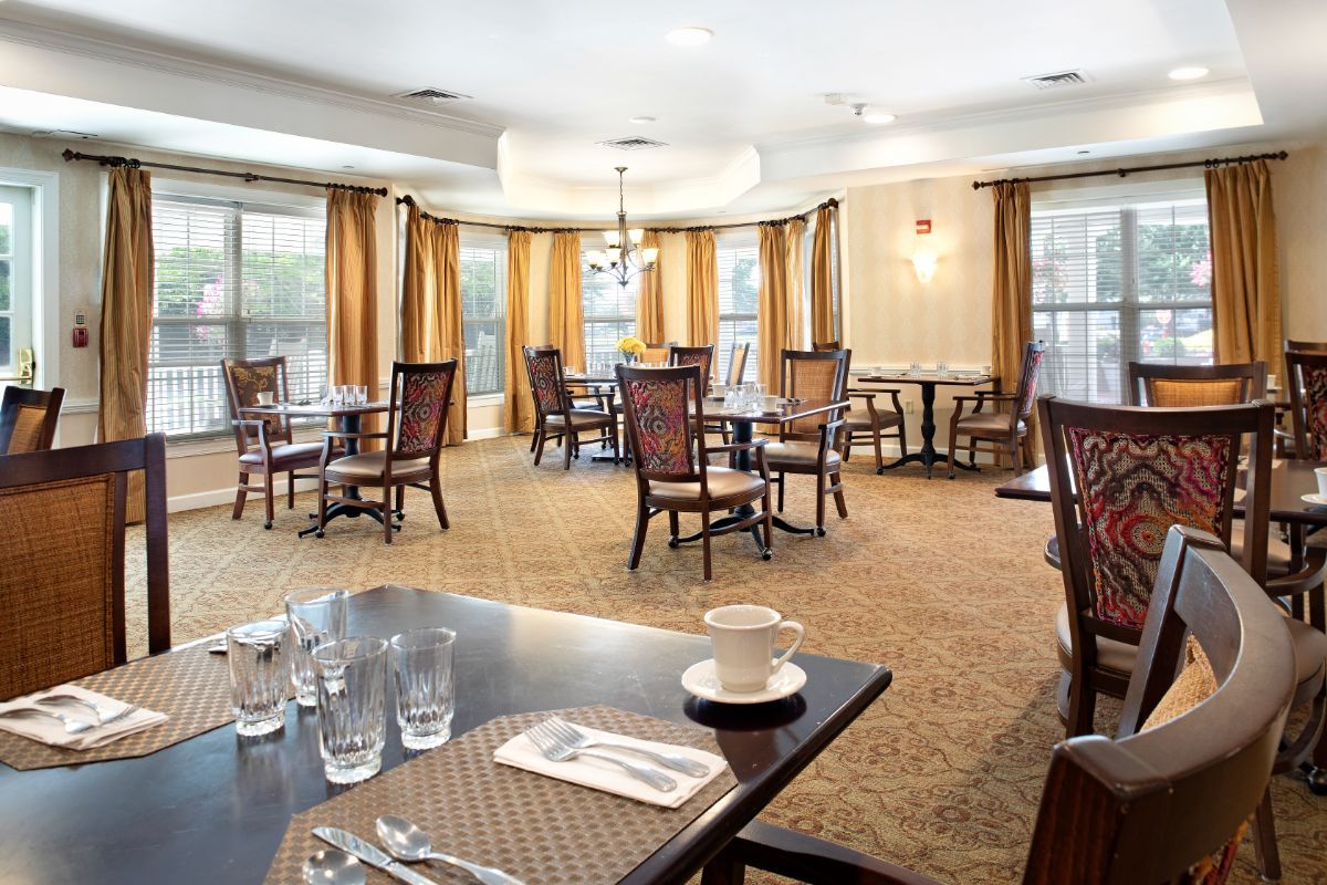 An elegant dining room with neatly arranged tables and chairs, featuring soft lighting and large windows with curtains.