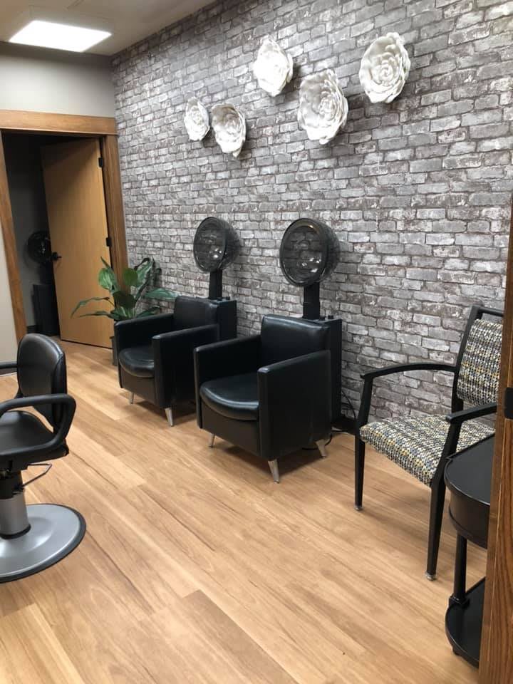 A modern salon interior with chairs and hair dryers against a brick wall backdrop.