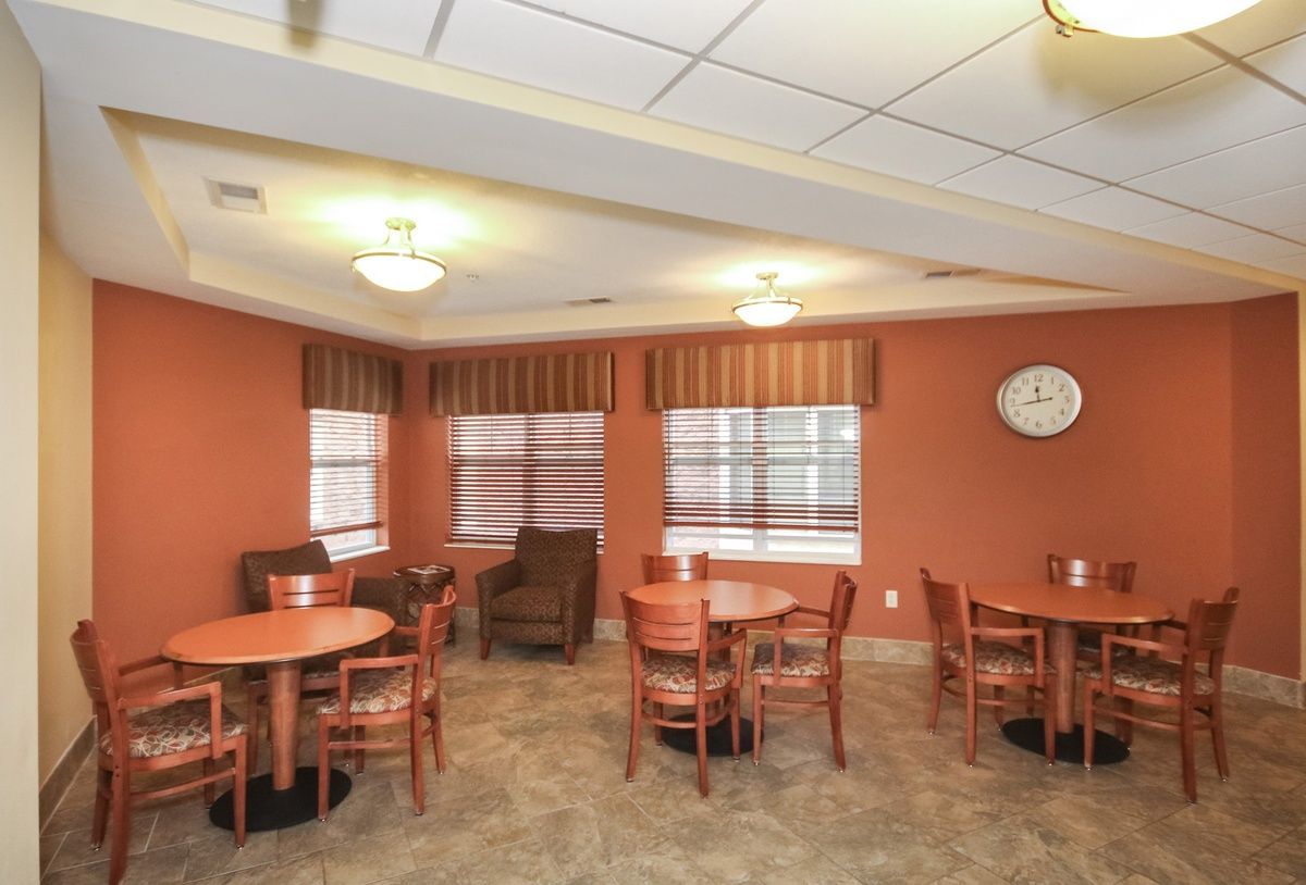 A cozy dining area with several tables and chairs, featuring soft lighting and a wall clock.