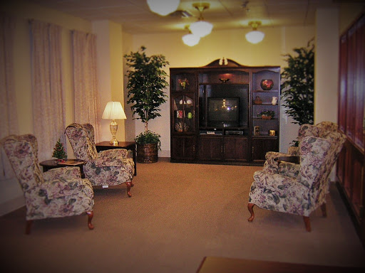 A cozy living room featuring floral-patterned chairs, a dark wooden television unit, and decorative plants.