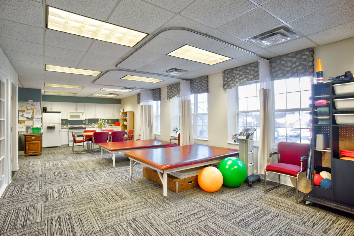 A bright and spacious physical therapy room equipped with tables, exercise balls, and chairs.