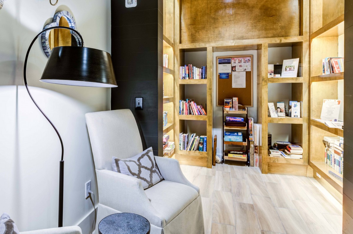 A cozy reading nook with a comfortable chair, floor lamp, and wooden bookshelves filled with various books.