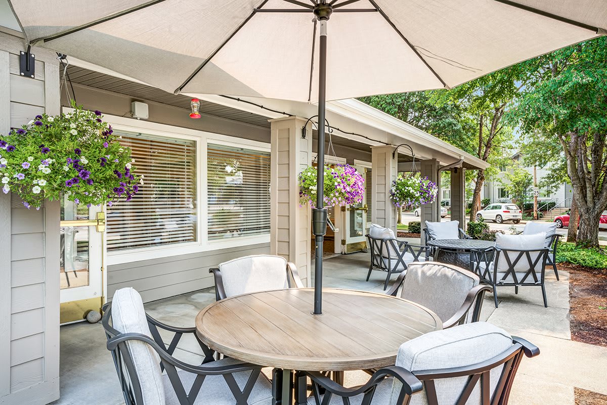 A cozy outdoor patio with tables and umbrellas, surrounded by greenery and flowers.