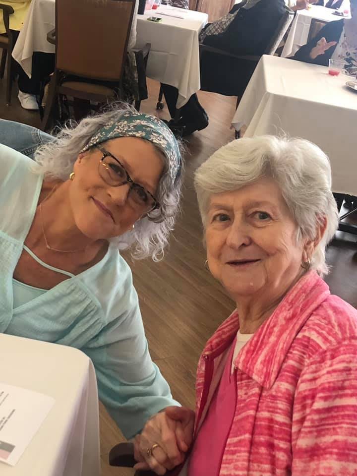 Two women smiling and sitting together indoors.