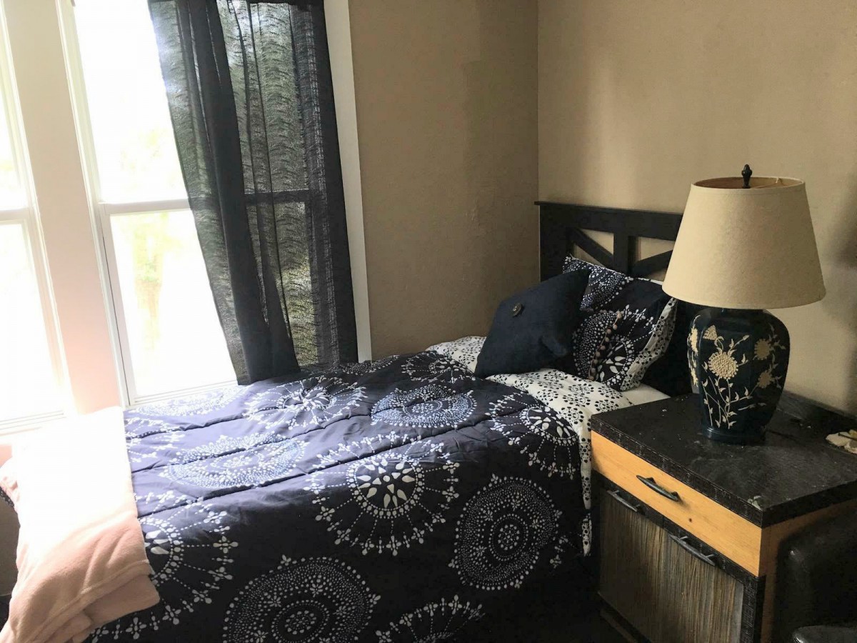 A cozy bedroom with a neatly made bed, decorative bedding, and a lamp on the nightstand beside a window.